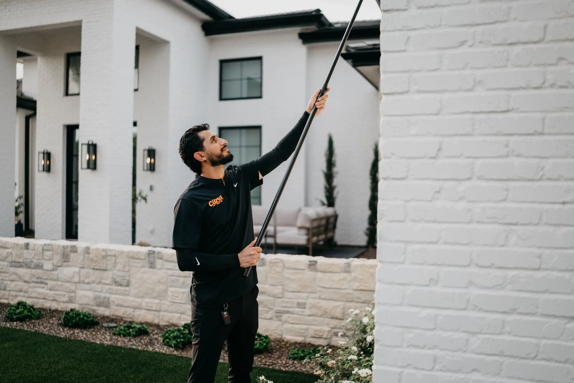 Citrus Pest Co technician using a long extension pole to clear spider webs from the eaves of an East Valley home
